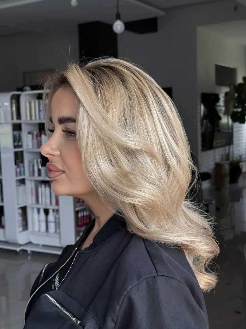 Klientka z jasnymi falami blond po koloryzacji, ujęcie z profilu w salonie