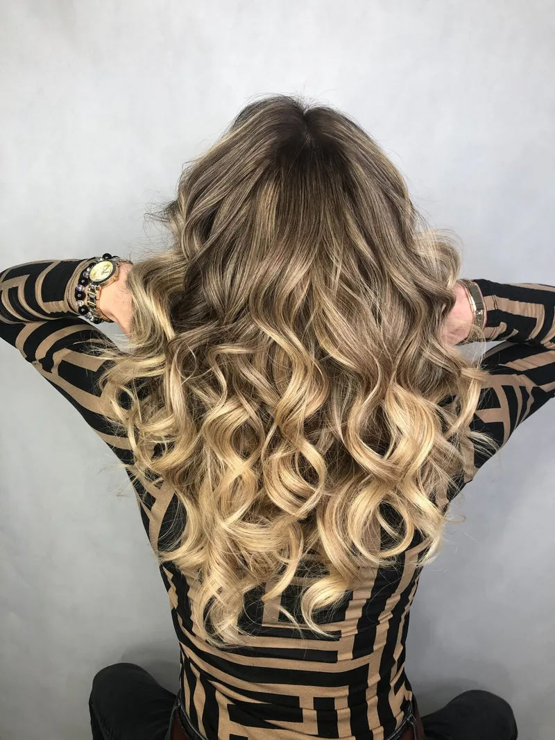 Miodowe blond loki z ciemniejszą nasadą, klientka odgarnia włosy, widok z tyłu